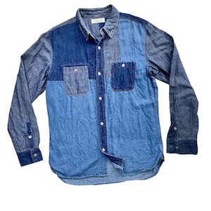 Op de afbeelding: Een denim shirt met lange mouwen in verschillende blauwtinten. Het shirt heeft een patchwork ontwerp met twee borstzakken en knoopsluitingen. De kraag heeft een klein label.