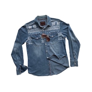 May include: A blue denim long-sleeved shirt with a white snowflake pattern and a red button fastening.
