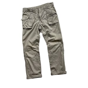 May include: Khaki-colored cargo pants with multiple pockets and a drawstring waist. The pants have button details on the knees and cuffed hems. The pants are made of a durable fabric.