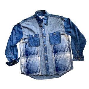 Peut inclure: Une chemise en jean bleu avec un motif pixelisé sur le devant. La chemise a un col boutonné et des manches longues.