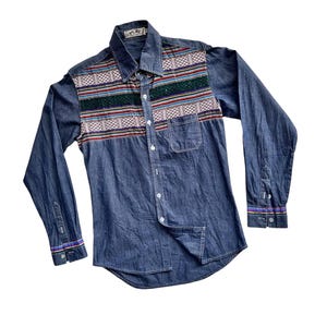 May include: A blue denim long-sleeve shirt with a colorful patterned yoke. The shirt has a button-up front and a single pocket on the left chest. The brand label reads "PLAY".