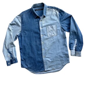 Op de afbeelding: Tweekleurig spijkeroverhemd met lange mouwen. Het overhemd heeft een gesplitst ontwerp, met één kant in donkerder blauwe denim en de andere in lichtere blauwe denim. Het heeft een knoopsluiting, een borstzak en manchetten met knopen. De merknaam "Niko and..." is zichtbaar.