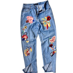 Könnte beinhalten: Hellblaue Jeans aus Denim mit gestickten Blumen- und geometrischen Applikationen in verschiedenen Farben, darunter Rot, Gelb, Pink und Blau. Die Jeans hat eine gerade Beinform und einen geteilten Saum.