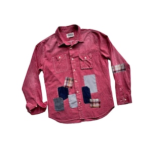 May include: A red long-sleeved button-down shirt with multiple fabric patches in various colors and patterns. The shirt has two chest pockets and a single brand label on the front.