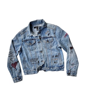May include: A light blue denim jacket with various black and white graphic designs and patches. The text "DO NOT DISTURB ME!" is written on the front of the jacket.