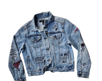 Könnte beinhalten: Eine hellblaue Jeansjacke mit verschiedenen schwarzen und weißen grafischen Designs und Patches. Der Text "DO NOT DISTURB ME!" ist auf der Vorderseite der Jacke geschrieben.