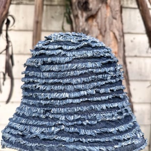 Peut inclure: Un chapeau de pêcheur en jean bleu avec un design à franges superposées. Le chapeau a une couronne arrondie et un petit bord. Les bords effilochés du denim créent un aspect texturé et décontracté.