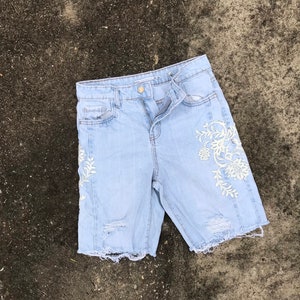 May include: Light blue denim shorts with white floral embroidery and distressed details.