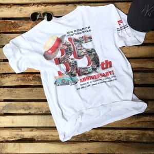 Puede incluir: Camiseta blanca con un gráfico rojo y negro de un coche y el texto "Mid America Motorworks 25th Anniversary! Funfest for Air-Cooled VW June 6-7, 2009 800.500.1500 www.mamotorworks.com"