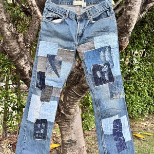 Könnte beinhalten: Blaue Jeans aus Denim mit einem Patchwork-Design aus verschiedenen blauen und grauen Stoffquadraten. Die Hose verfügt über sichtbare weiße Nähte, ausgefranste Kanten an den Flicken und eine klassische Fünf-Taschen-Konstruktion mit Knopfverschluss.