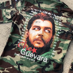 May include: A camouflage green jacket with a portrait of Che Guevara printed on the back. The jacket has a red star and the text "Che Guevara Ernesto Guevara de la Serna" printed below the portrait. The text "The road is long and the well read is long and full of difficulties. At times we wander must turn..." is printed around the portrait.