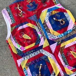 May include: A red, yellow, blue, and white patchwork vest with embroidered snakes and birds. The vest is made of different fabrics and has a gingham pattern on the bottom.