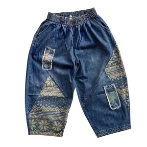 Op de afbeelding: Blauwe spijkerbroek met een patchwork-ontwerp. De broek heeft een wijde pijp en een ontspannen pasvorm. De patchwork omvat een bloemenprint, een geometrisch patroon en een ruitpatroon.