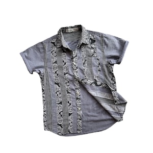 Könnte beinhalten: Ein kurzärmeliges Hemd mit Knöpfen und Patchwork-Design. Das Hemd ist aus hellblauem Stoff und hat schwarze und weiße Paisley- und Karomuster.