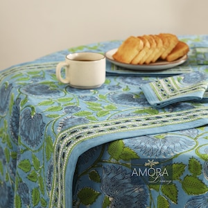 May include: A blue and green floral tablecloth with a white border. The tablecloth is set with a cup of coffee and a plate of toast.