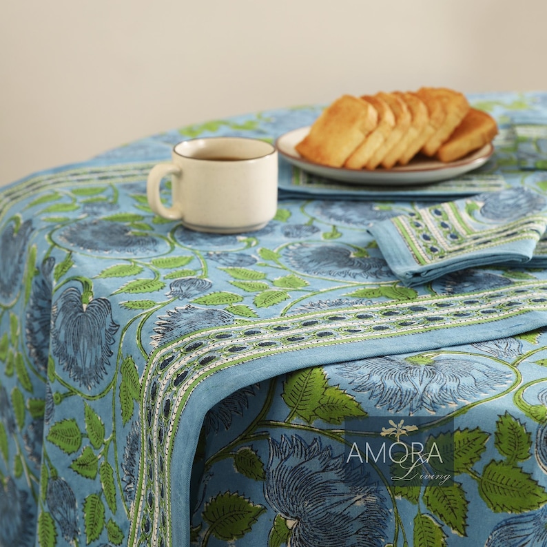 May include: A blue and green floral tablecloth with a white border. The tablecloth is set with a cup of coffee and a plate of toast.