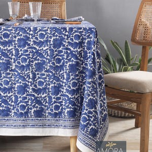 Könnte beinhalten: Eine weiße Tischdecke mit einem blauen Blumendesign und einem weißen Rand. Die Tischdecke liegt auf einem Holztisch mit zwei Stühlen. Die Stühle sind aus Holz und haben geflochtene Rohrseats. Die Tischdecke ist aus Baumwolle und perfekt für ein zwangloses Esszimmer.