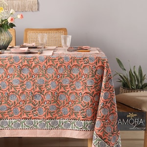 May include: A pink and blue floral tablecloth with a green border. The tablecloth is laid on a table with two chairs and a vase of flowers.