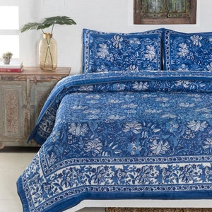 May include: A blue and white floral patterned quilt set on a bed. The quilt and pillowcases feature a detailed botanical design. The color palette includes shades of blue and white, creating a calming aesthetic. The bedding is neatly arranged, suggesting a comfortable bedroom setting.