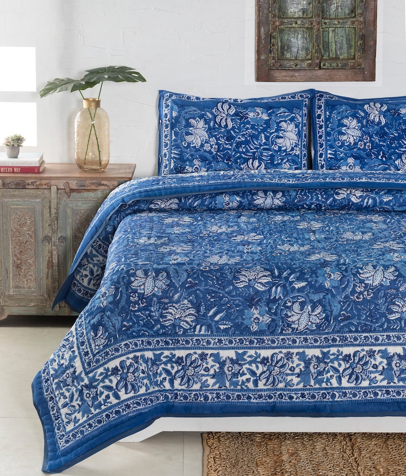 May include: A blue and white floral patterned quilt set on a bed. The quilt and pillowcases feature a detailed botanical design. The color palette includes shades of blue and white, creating a calming aesthetic. The bedding is neatly arranged, suggesting a comfortable bedroom setting.