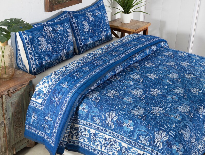 May include: A blue and white floral patterned quilt set. The bedding includes a quilt and two pillow shams. The design features a detailed floral pattern in shades of blue and white, creating a cohesive and decorative bedroom set.