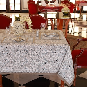 May include: A white tablecloth with a blue and gray floral pattern. The tablecloth is laid on a table with place settings and a decorative lantern.