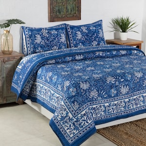 May include: A blue and white floral patterned quilt set on a bed. The set includes a quilt and two pillow shams. The quilt features a detailed floral design with a white border. The bedding is made of a soft material.