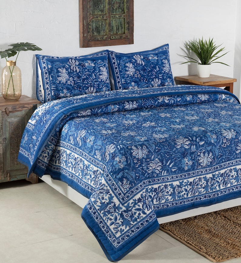 May include: A blue and white floral patterned quilt set on a bed. The set includes a quilt and two pillow shams. The quilt features a detailed floral design with a white border. The bedding is made of a soft material.