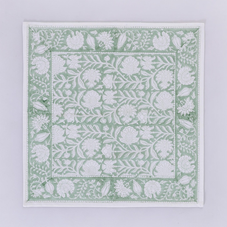 Pode incluir: Um tapete de mesa quadrado de tecido verde e branco com um padr&atilde;o floral. O tapete de mesa tem uma borda branca com um design floral.