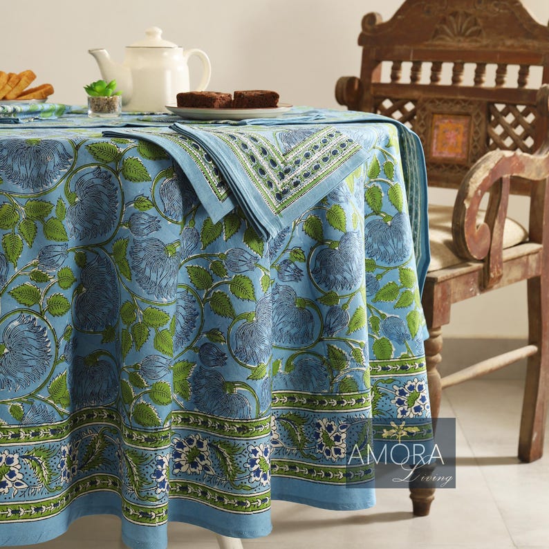 May include: A blue and green floral patterned tablecloth with a white border. The tablecloth is laid on a round table with a wooden chair beside it.