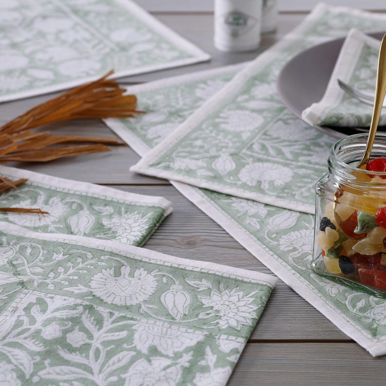 Pode incluir: Conjunto de quatro  placemats com padr&atilde;o floral verde e branco. Os placemats s&atilde;o feitos de algod&atilde;o e t&ecirc;m um brilho sutil. Os placemats est&atilde;o dispostos em uma mesa de madeira.
