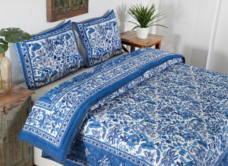 May include: A blue and white floral patterned quilt and two matching pillow shams rest on a bed. The bedding features a detailed floral design with a solid blue border. The room has a rustic, bohemian aesthetic.