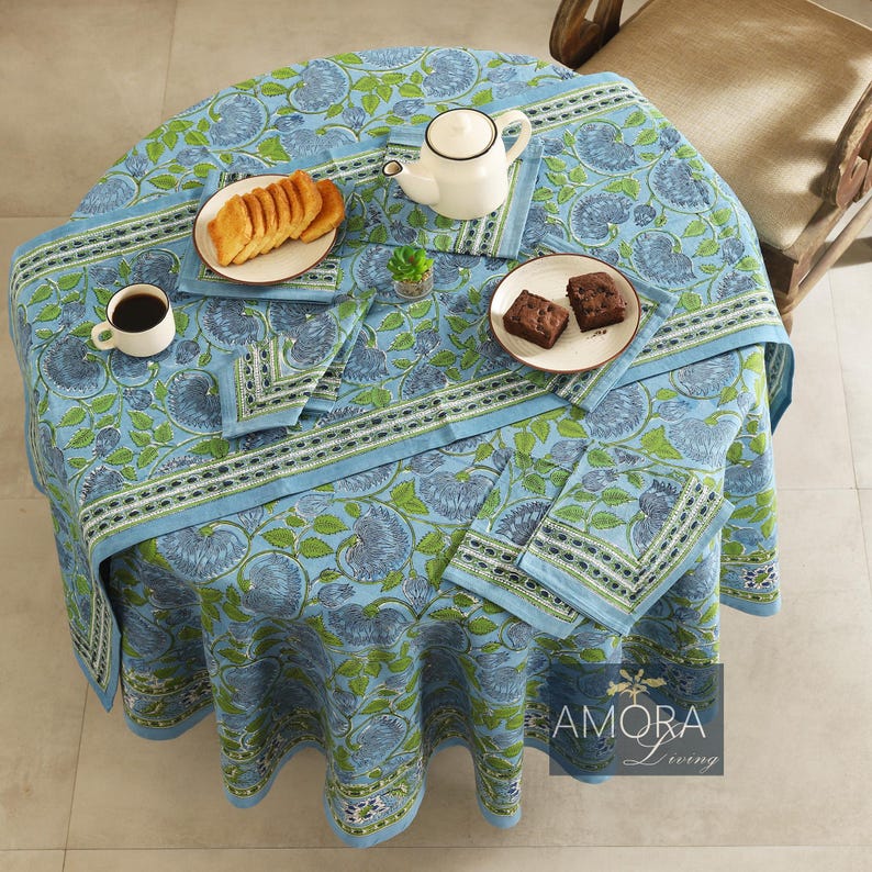 May include: A blue and green floral tablecloth with a white border and a matching set of napkins. The tablecloth is laid out on a table with a cup of coffee, a plate of cookies, and a plate of brownies.