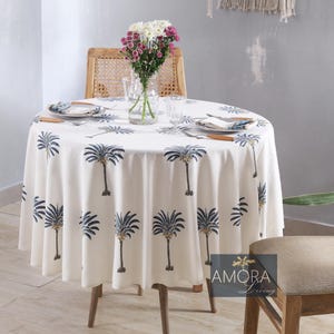 May include: A white round tablecloth with a palm tree print in blue and yellow. The tablecloth is set on a round table with two place settings and a vase of flowers.
