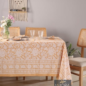 Può includere: Una tovaglia beige con un motivo floreale bianco e un bordo di motivi paisley bianchi. La tovaglia è stesa su un tavolo di legno con quattro sedie. Il tavolo è apparecchiato con piatti, posate e bicchieri. La tovaglia è in cotone e lavabile in lavatrice.