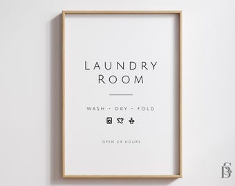 May include: A white framed sign with the text "Laundry Room" in black lettering. Below the text is "Wash - Dry - Fold" with laundry symbols for washing, drying, and hanging clothes. The sign also says "Open 24 Hours".