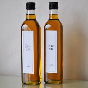 Pode incluir: Duas garrafas de vidro de azeite de oliva com tampas pretas e etiquetas brancas. As etiquetas têm o texto "Olive Oil" e "Oils & Vinegars".