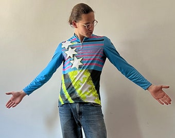 Può includere: Una persona indossa una camicia a maniche lunghe blu, bianca e rosa con una stampa grafica di stelle e strisce. Indossa anche jeans blu e scarpe da ginnastica nere e viola.