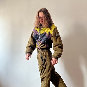 May include: A person wearing a green and yellow ski suit with a geometric pattern. The suit has a zipper down the front and a hood. The person is wearing black sneakers.