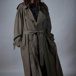 Könnte beinhalten: Olivgrüner Trenchcoat mit doppelreihigem Design, Taillengürtel und Knopfdetails. Der lange Mantel hat eine klassische Silhouette und ist aus strapazierfähigem Stoff gefertigt. Vielseitige Oberbekleidung.