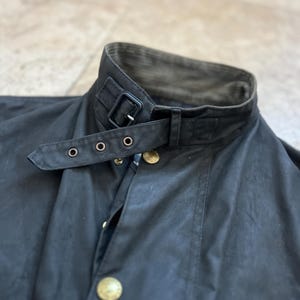 Peut inclure: Une veste en coton cir&eacute; noir avec un col en velours c&ocirc;tel&eacute; et une sangle &agrave; boucle noire. La veste a une fermeture &agrave; boutons et deux poches.