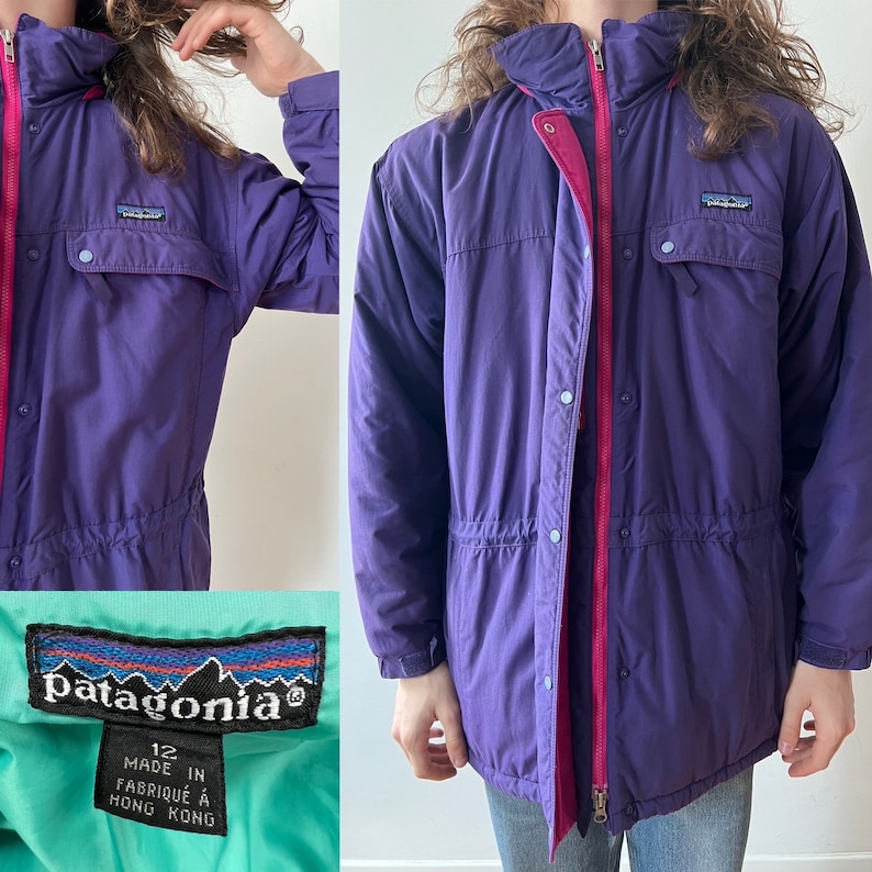 Pu&ograve; includere: Giacca Patagonia viola con cerniera rosa e un'etichetta blu chiaro che dice "Patagonia" e "12 Made in Hong Kong".