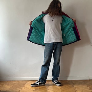 Pu&ograve; includere: Una giacca imbottita multicolore con fodera turchese. La giacca &egrave; aperta e la persona che la indossa &egrave; di spalle alla telecamera.