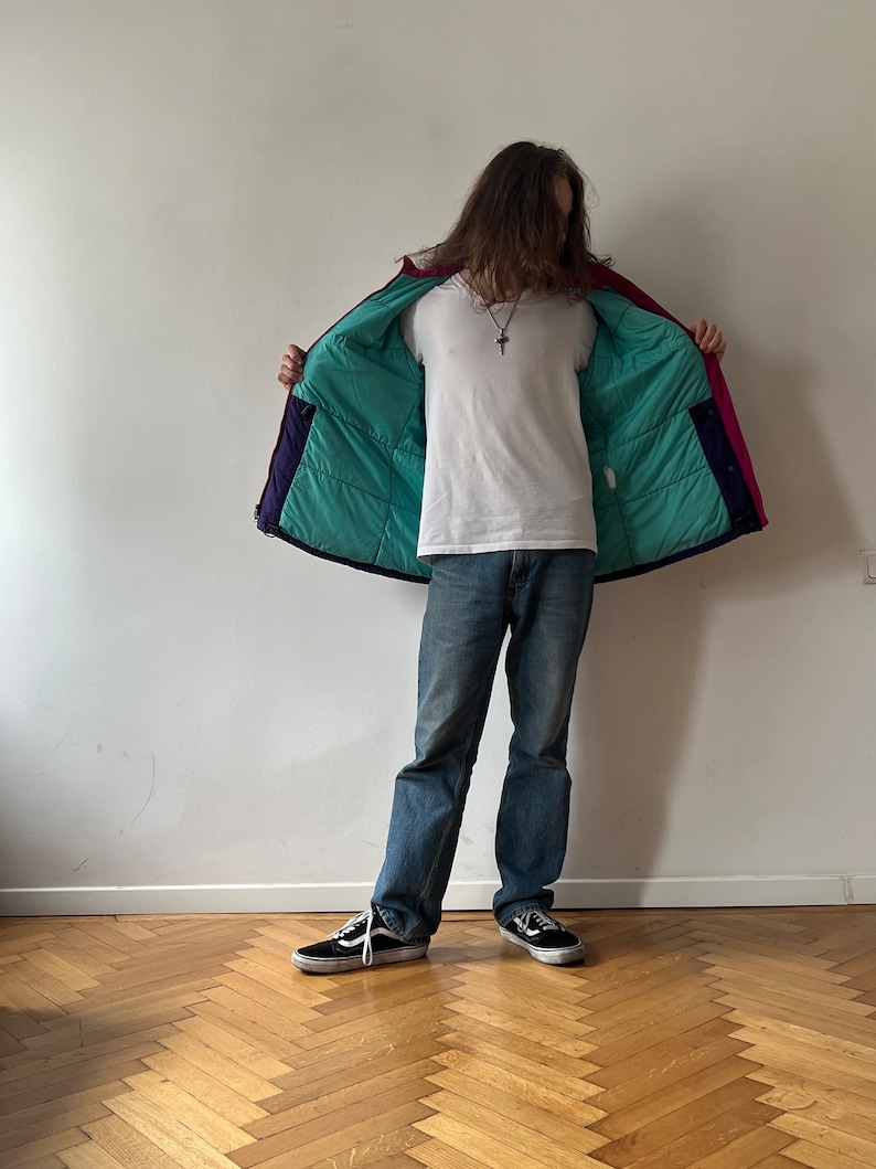 Pu&ograve; includere: Una giacca imbottita multicolore con fodera turchese. La giacca &egrave; aperta e la persona che la indossa &egrave; di spalle alla telecamera.