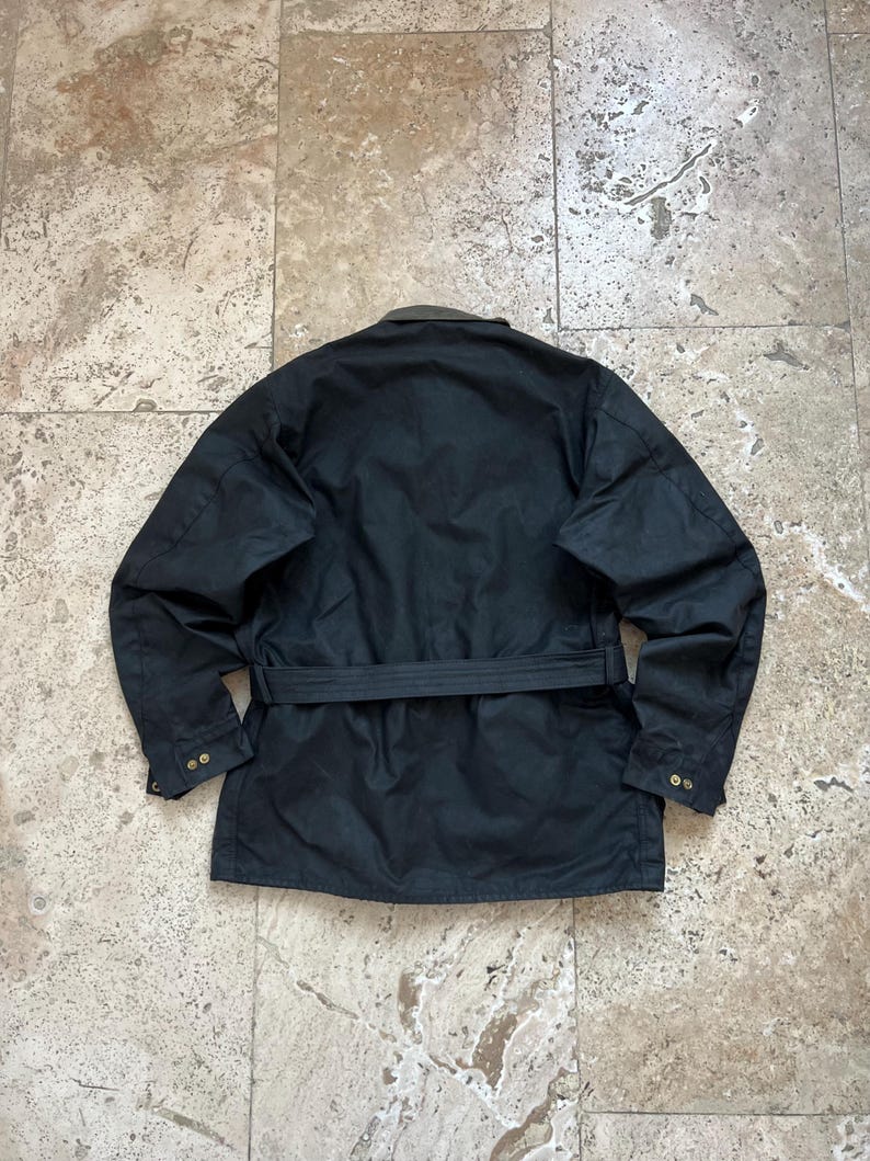 Peut inclure: Une veste noire ceintur&eacute;e avec un col marron et deux boutons de fermeture sur chaque poignet.