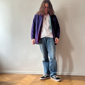 Pu&ograve; includere: Una persona che indossa una giacca viola e rossa con una maglietta bianca, jeans blu e scarpe da ginnastica nere.