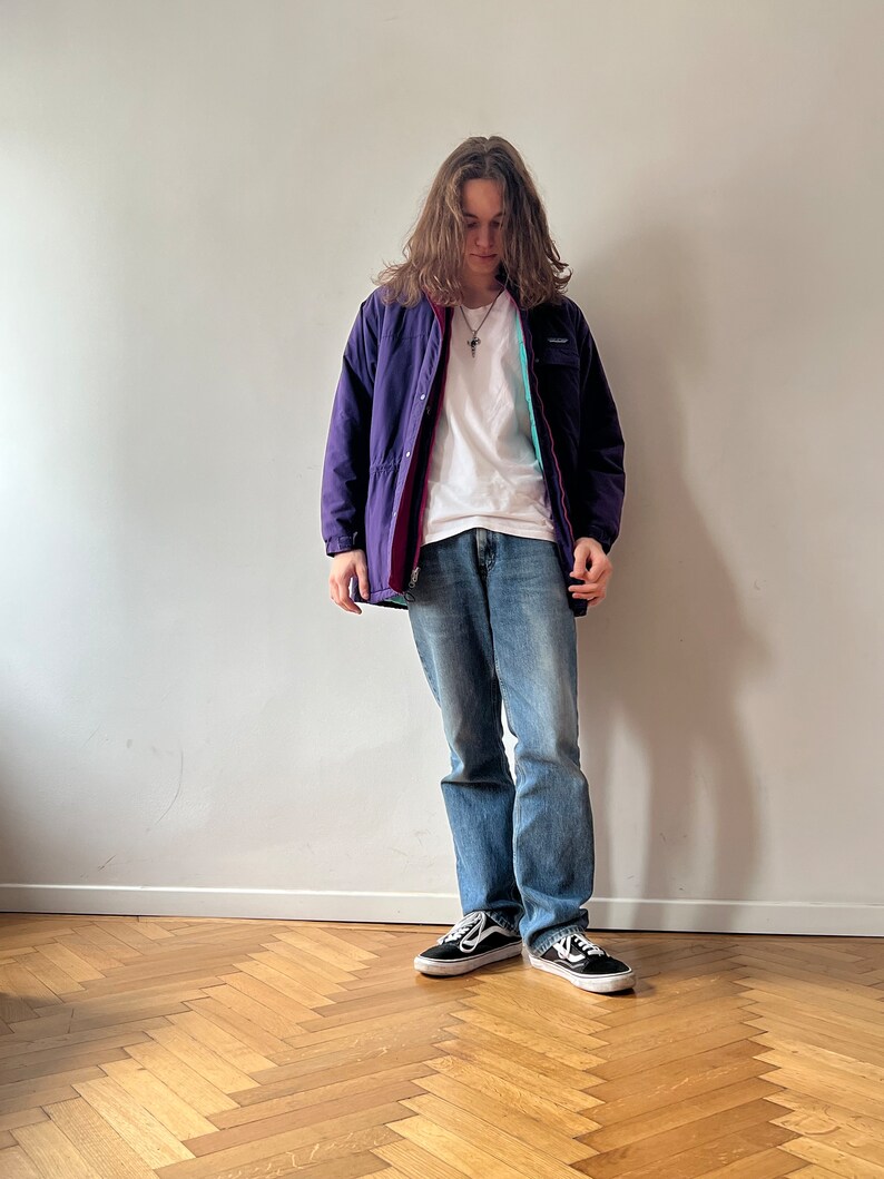 Pu&ograve; includere: Una persona che indossa una giacca viola e rossa con una maglietta bianca, jeans blu e scarpe da ginnastica nere.