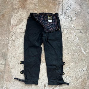 Peut inclure: Pantalon en coton cir&eacute; noir Barbour avec des bretelles r&eacute;glables et une doublure en tartan. Le pantalon a deux grandes poches sur le devant et deux petites poches &agrave; l'arri&egrave;re.