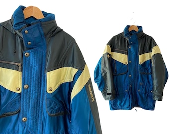 以下が含まれることがあります： 右袖に「Descente」と書かれた青、黒、黄色のスキー用ジャケットです。