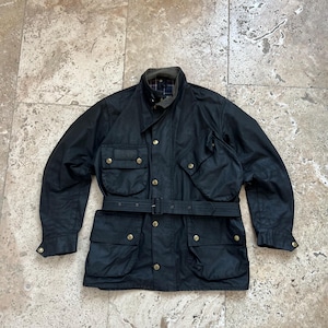 Peut inclure: Une veste en coton cir&eacute; noir avec une ceinture, plusieurs poches et des boutons en laiton.